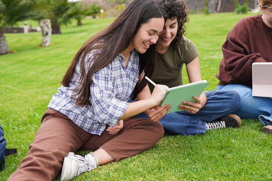 Young people studying outside of school building sitting on meadow and using digital tablet - Generation z students, education and university concept