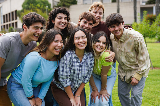Group of diverse university students smiling and hugging each other in front of camera outside of school building - Back to school, young people and education concept