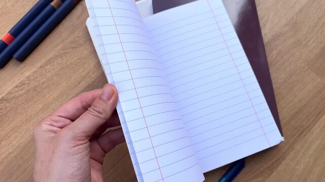 Hand turning blank pages of lined notebook on wooden desk, cozy lifestyle, daily planning.