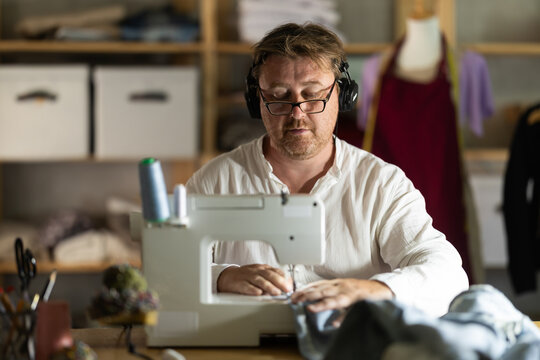 Middle-aged male dressmaker with headphones working with sewing-machine