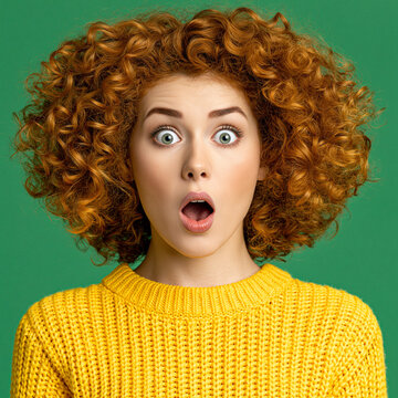 Shocked young woman with curly red hair and yellow sweater against green