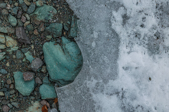 dettaglio di ciottoli e rocce levigate di colore verde-azzurro adiacenti a una superficie coperta di neve e ghiaccio in un ambiente naturale di montagna in inverno