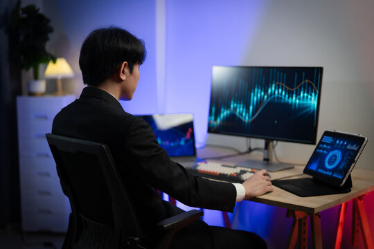 Asian Businessman Trading Stocks and Analyzing Financial Data Charts on Multiple Screens in Dark Office at Night