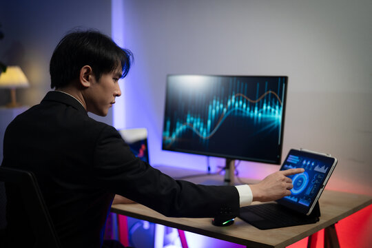Asian Businessman Trading Stocks and Analyzing Financial Data Charts on Multiple Screens in Dark Office at Night
