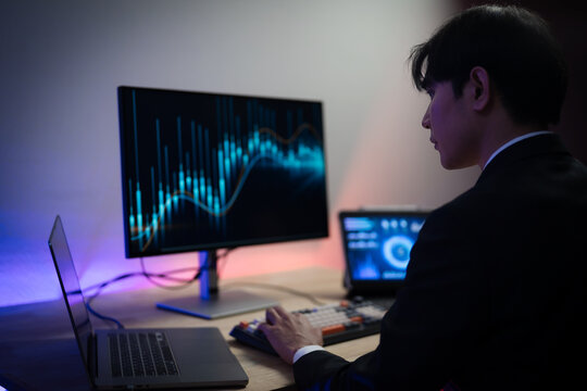 Asian Businessman Trading Stocks and Analyzing Financial Data Charts on Multiple Screens in Dark Office at Night