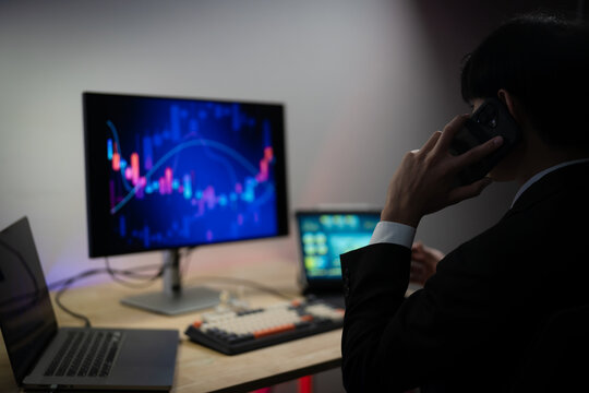 Asian Businessman Trading Stocks and Analyzing Financial Data Charts on Multiple Screens in Dark Office at Night