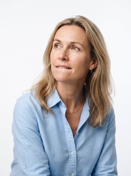 Thoughtful middle aged woman with blonde hair biting her lip and looking up against a white background