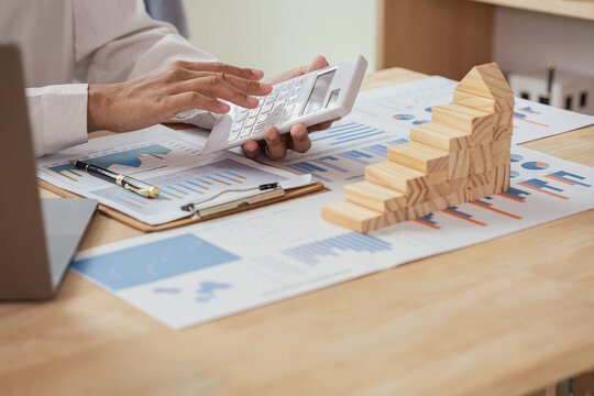 Businessman Using Calculator to Calculate Financial Growth, Investment Strategy and Mortgage Planning with Wooden Block House Stairs