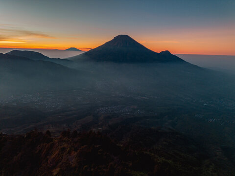 A panoramic view of Mount Sindoro set against a golden-blue sky at sunrise. Rising over 3,000 meters above sea level, the mountain looks majestic and beautiful on a clear morning.