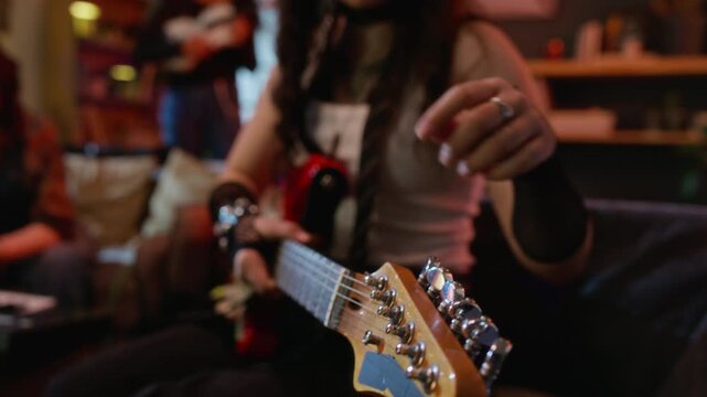 Young woman tuning red electric guitar during rehearsal session, close-up on headstock. Clip is ideal for music education platforms, hobbyist lifestyle ads, and creative arts promotions
