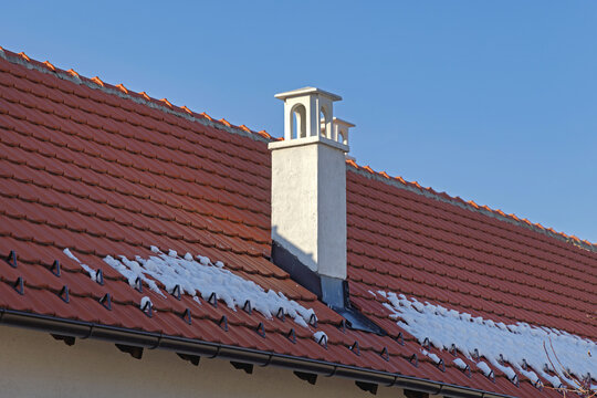 White Chimney With Ornate Cap at Red Tiled Roof Covered With Snow Cold Winter Day