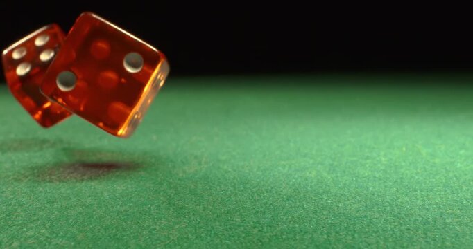 Dice fly and tumble toward the camera in extreme slow motion, landing on a green casino table with
