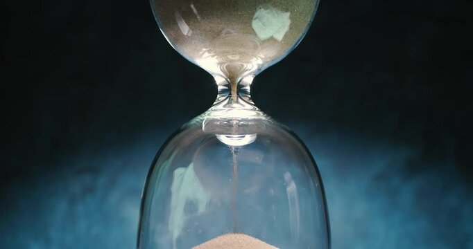 Hourglass with flowing sand on dark background.Shot on super slow motion camer.
