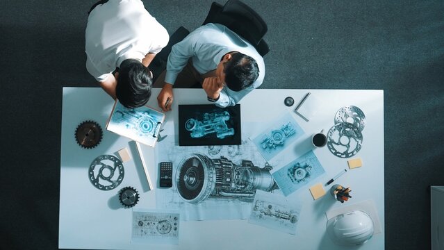 Top down aerial view of smart manager sitting while colleague walking at meeting. Professional engineer looking at turbine engine or electronic generator while colleague asking question. Alimentation.