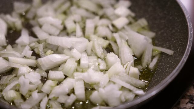 Chopped onion sauteing in olive oil in pan close-up. Fresh onion frying in olive oil in pan.