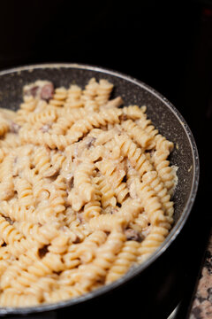 Fusilli pasta cooking in creamy mushroom sauce in pan.