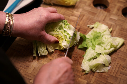 Cutting lettuce head with knife on wooden cutting board. Woman cutting fresh lettuce.