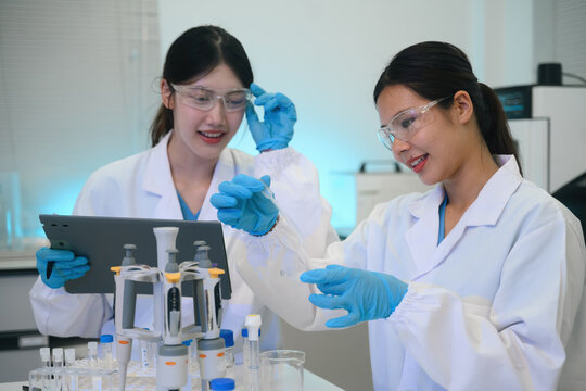 Two Asian Female Scientists Collaborating in Modern Laboratory with Pipettes and Test Tubes