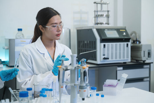 Asian Female Scientist Working in Modern Laboratory with Pipette and Digital Tablet