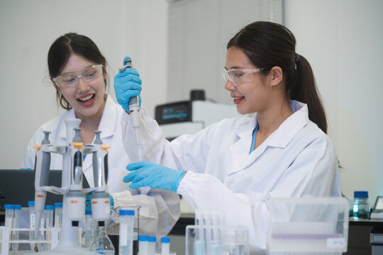 Two Happy Asian Female Scientists Working Together in Laboratory Using Pipette and Lab Equipment