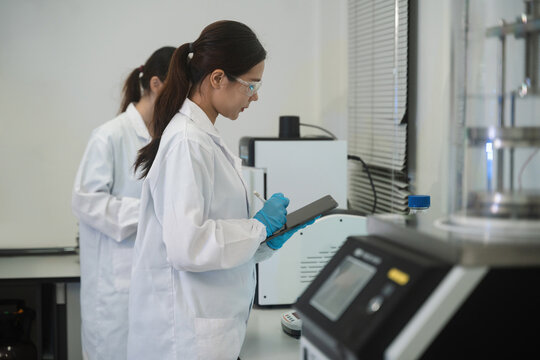 Female Scientists in White Lab Coats Working with Equipment and Tablet in Modern Laboratory