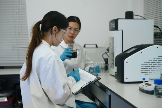Two Asian Female Scientists Working in Laboratory, Recording Data and Examining Chemical Sample