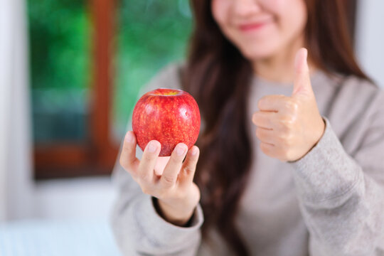 Closeup image of a woman showing thumbs up hand sign while holding a red apple