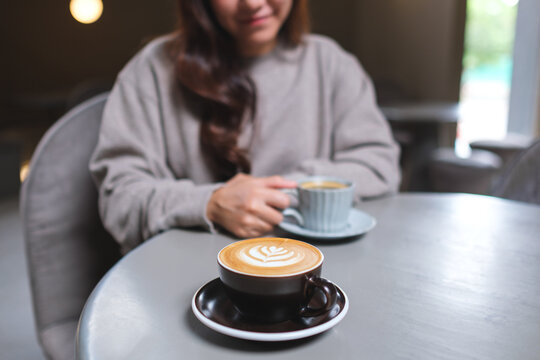 Closeup image of a woman holding and drinking coffee with friend in cafe