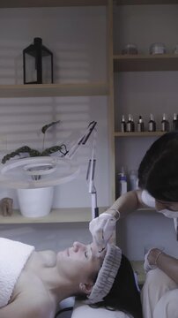 Steady hand guides fine tool along closed eyelid in calm skincare session