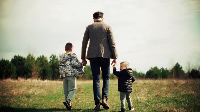 Father Walking Hand In Hand With Children Across Open Field Landscape 
