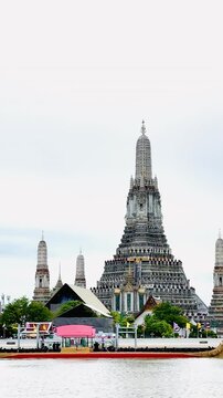 A golden Thai royal barge processional rowing past the iconic Wat Arun temple on the Chao Phraya River in Bangkok, Thailand during a traditional cultural ceremony under a bright daylight sky.