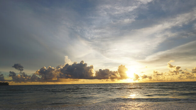 Dramatic sunset over the ocean with golden sunlight, dark storm clouds and shimmering waves