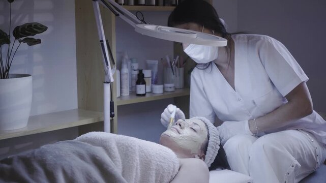 Gloved esthetician applying gentle facial treatment beneath a bright lamp