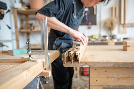 Skilled craftsman in restoration studio working on wooden patch on window frame at workstation, master during renovation preparatory work, selection of wood grain of same type, hardness and age.