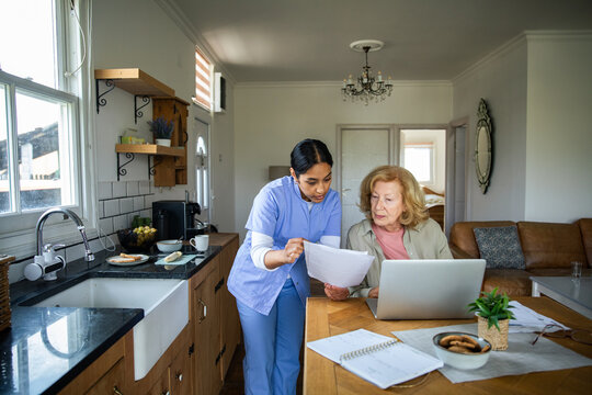 Caregiver helping senior with paperwork at home kitchen