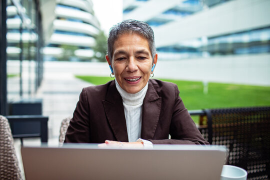 Senior businesswoman video calling on laptop at modern office courtyard