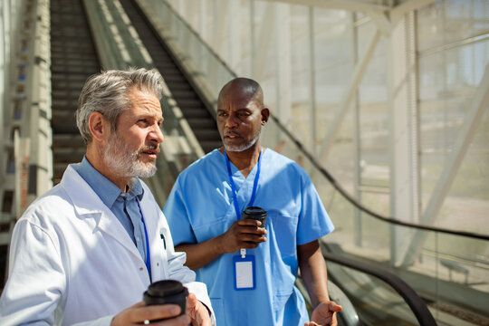 Male medical professionals talking over coffee in hospital corridor