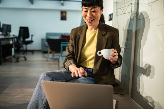 Smiling businesswoman video calling with coffee in modern office