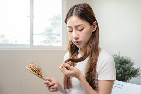 Hair fall problem concept. Shocked Asian woman looking at many hair lost in her hand and comb.