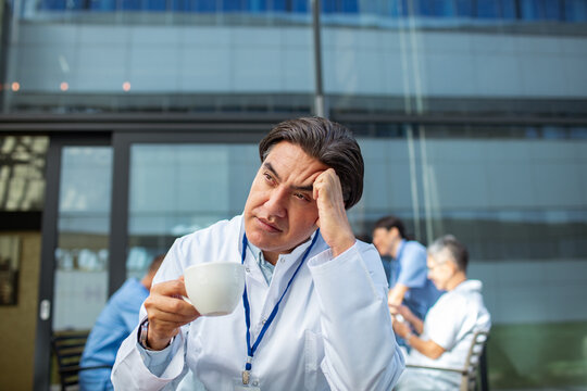 Stressed doctor drinking coffee during hospital break outdoors