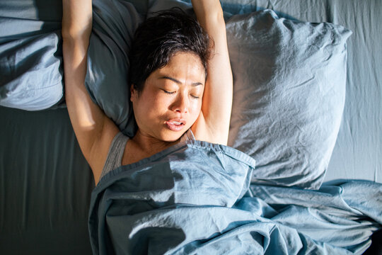 Woman waking up and stretching in bed at home