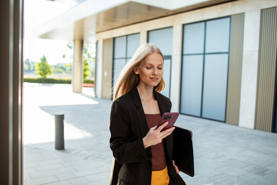 Young businesswoman checking smartphone outside office