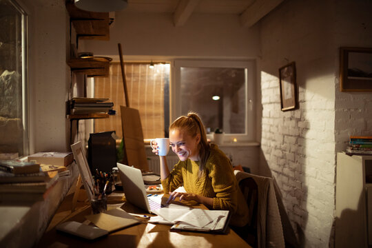 Smiling woman working late on laptop at home office