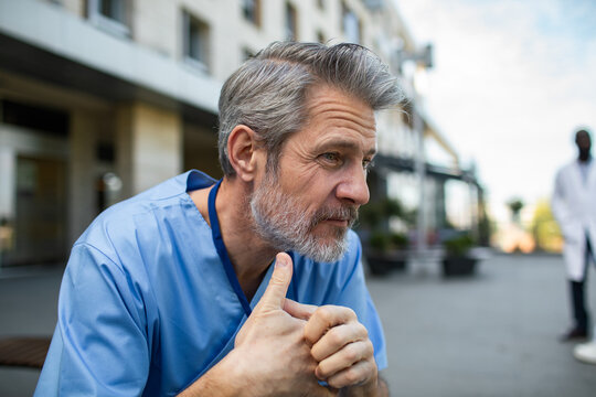 Mature healthcare worker in scrubs resting outside hospital