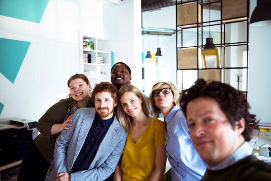 Diverse coworkers taking a group selfie in modern office