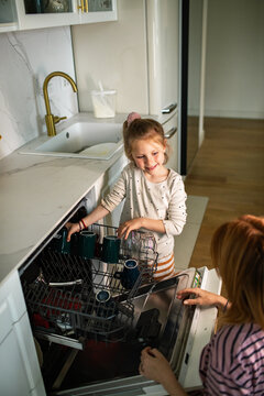 Smiling girl loading a dishwasher with parent at home