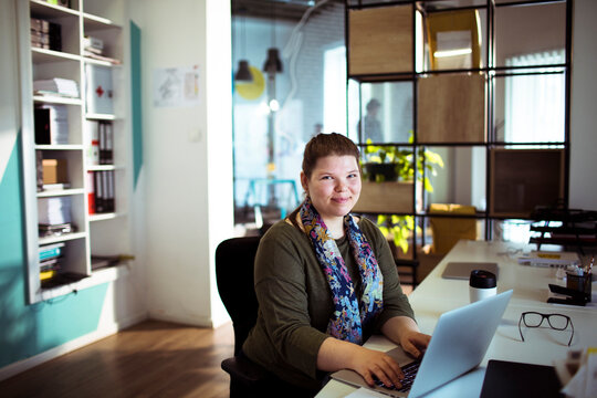 Smiling professional woman working on laptop in modern coworking office