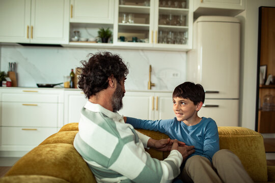 Father and son talking on yellow sofa in modern kitchen