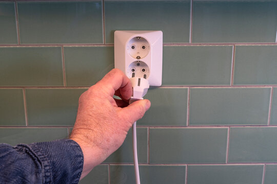 Hand of unrecognizable person connecting electric plug in outlet on wall