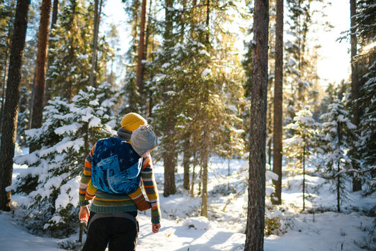 Mother carrying toddler on back while standing in winter forest
